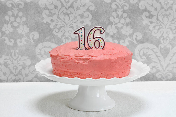 Bolo rosa de camada de aniversário fosco com o número 16 no topo em um suporte de bolo de pedestal branco. Espaço para cópia. Pronto para suas decorações
. - Foto, Imagem