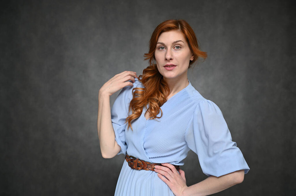 The model shows different emotions. Portrait of a young pretty red-haired actress woman in a blue dress on a gray background. - Φωτογραφία, εικόνα