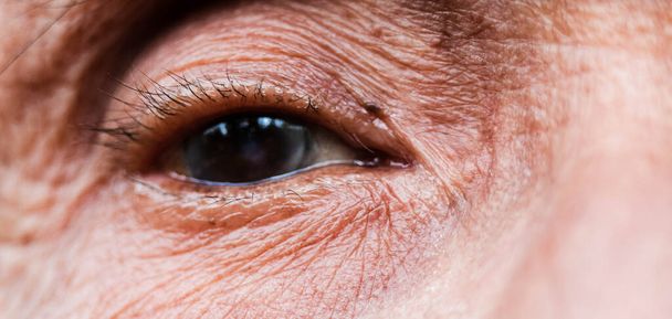 Primer plano de un ojo de un anciano asiático con arrugas alrededor de los ojos
. - Foto, Imagen