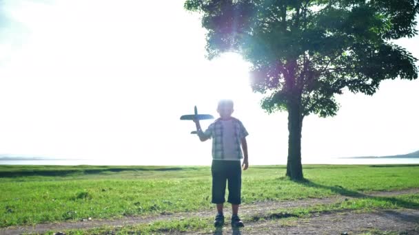 Šťastné asijské dítě chlapec házejí hrát letadlo simulovat v přírodě, stromy a travnaté porosty venku, který má sluneční světlo ve večerních hodinách. Šťastná dovolená Pomalý pohyb - Záběry, video