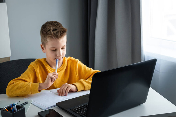 Distance learning, a boy learns math while looking at a laptop beech during an online lesson. The concept of online education, home education, technology, quarantine, self-isolation - Fotoğraf, Görsel