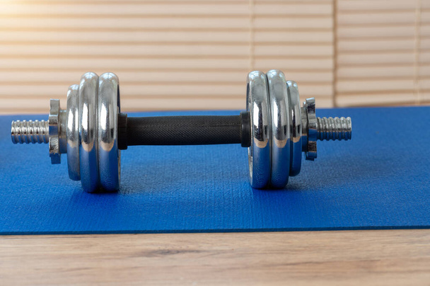 Manubri in ferro argentato messi su un tappetino blu per giocare a fitness all'interno della casa su un pavimento in legno. - Foto, immagini