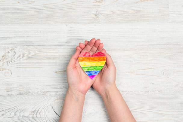Female hands hold rainbow LGBT heart on a  light wooden table. Homosexual and lgbt concept. - Photo, image