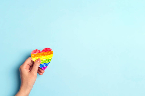 Female hand hold rainbow LGBT heart on a blue background. Copy space for text. Homosexual and lgbt concept. - Fotó, kép