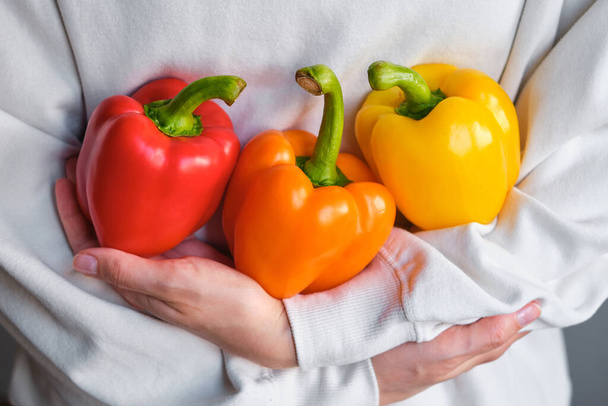 The girl holds colored bell pepper in her hands. Ripe fresh big sweet pepper. Healthy food, organic vegetables. Natural vitamins, raw ingredient for eating. Handpicked bio capsicum - Foto, Bild