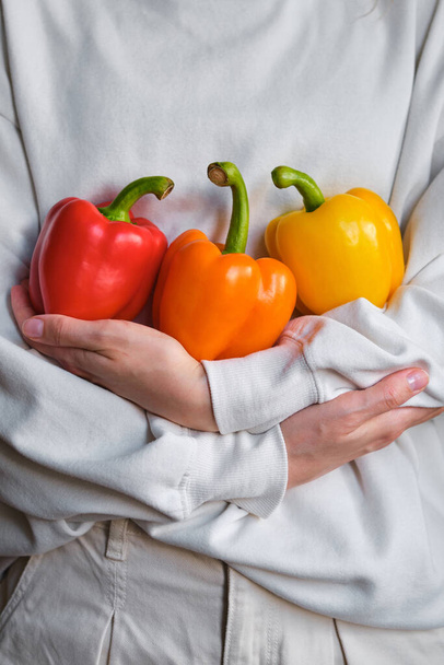 The girl holds colored bell pepper in her hands. Ripe fresh big sweet pepper. Healthy food, organic vegetables. Natural vitamins, raw ingredient for eating. Handpicked bio capsicum - Фото, изображение