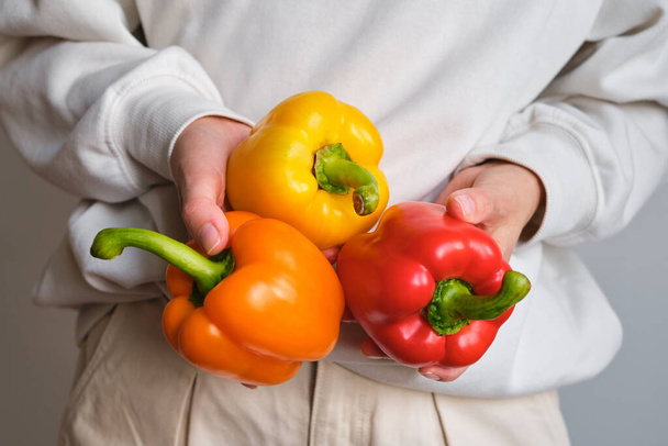 The girl holds colored bell pepper in her hands. Ripe fresh big sweet pepper. Healthy food, organic vegetables. Natural vitamins, raw ingredient for eating. Handpicked bio capsicum - Photo, image