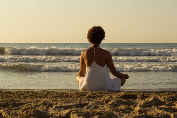 Czarna Afroamerykanka myśląca na plaży o wschodzie słońca w białej sukience. medytacja - Zdjęcie, obraz