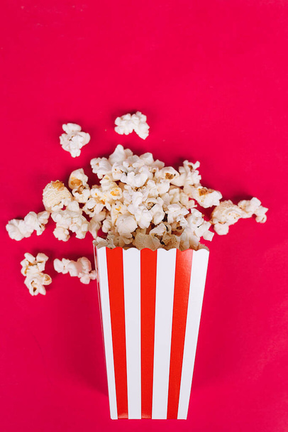 Popcorn in cardboard box on red background Conceptual cinema, watch a movie - Foto, afbeelding