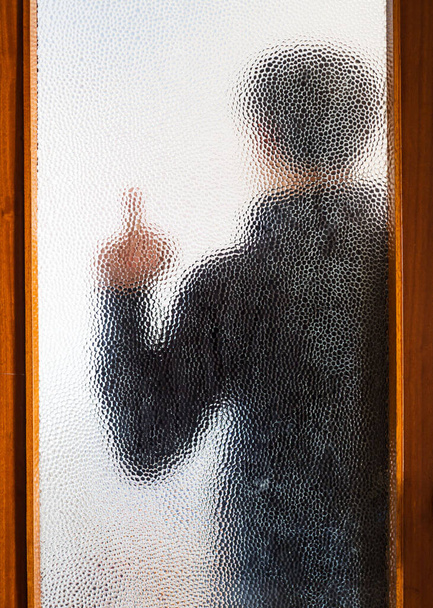 Homem de preto atrás da porta fechada através de vidro
 - Foto, Imagem