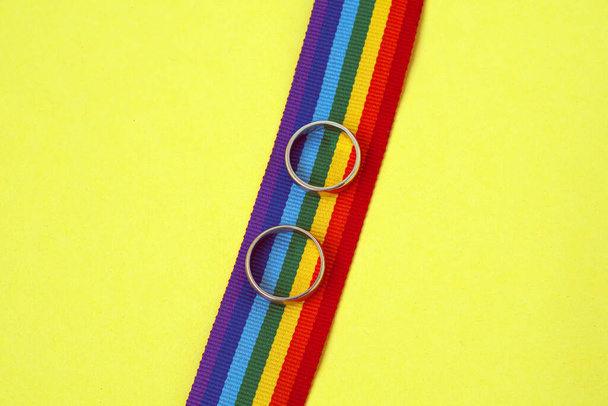 pair of white golden wedding rings on LGBTQ rainbow ribbon on yellow background - Photo, image