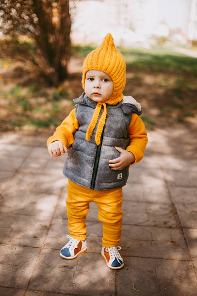 Stylish little one-year-old boy in a yellow hat, yellow pants and a gray jelly on the background of nature - Φωτογραφία, εικόνα