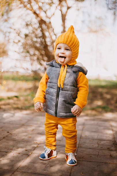 Stylish little one-year-old boy in a yellow hat, yellow pants and a gray jelly on the background of nature - Foto, Bild