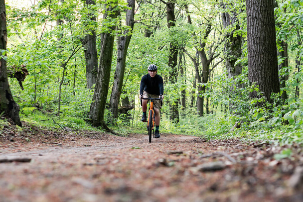 Um jovem da parte de trás montando uma bicicleta ao longo do caminho entre as árvores ao lado do lago
 - Foto, Imagem