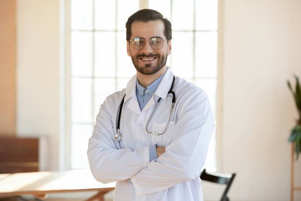 Porträt eines lächelnden kaukasischen Arztes, der am Arbeitsplatz posiert - Foto, Bild