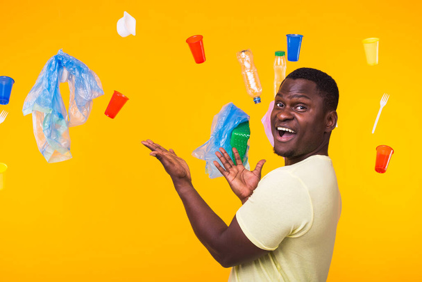 世界環境デー、プラスチックリサイクルの問題と環境災害の概念-黄色の背景にゴミを見て驚くアフリカ系アメリカ人の男性. - 写真・画像