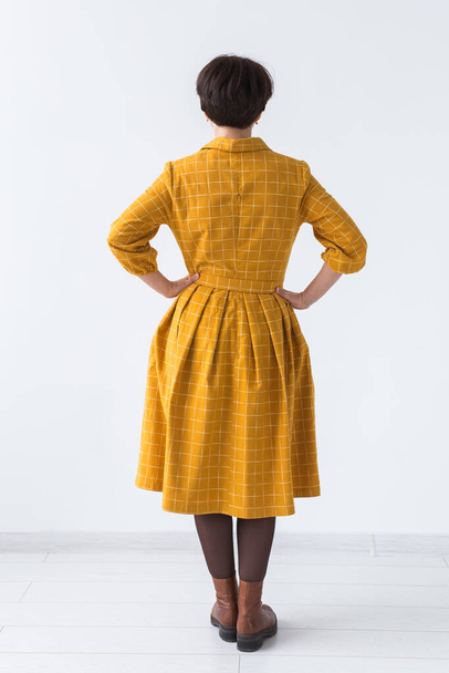concept de vêtements, designer, personnes - vue arrière de la femme attrayante dans une robe jaune posant sur la chambre blanche
. - Photo, image