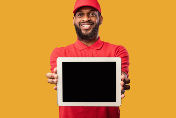 Courier Showing Tablet Screen Recommending Delivery Service Over Yellow Background - Foto, imagen