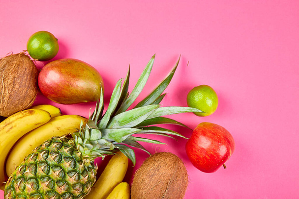 Flat lay of exotic fruits on pink background - mango, pineapple, banana, avocado, coconut, lime. Top view. Creative layout made of tropical fruits, copy space, summer concept. - Foto, Imagem