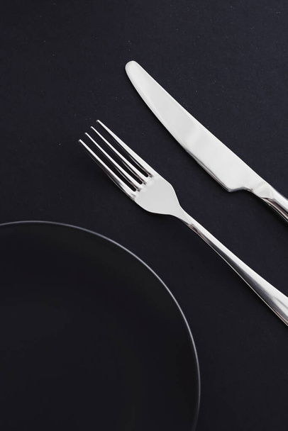 Leere Teller und Besteck auf schwarzem Hintergrund, hochwertiges Geschirr für Festtagsessen, minimalistisches Design und Ernährung - Foto, Bild