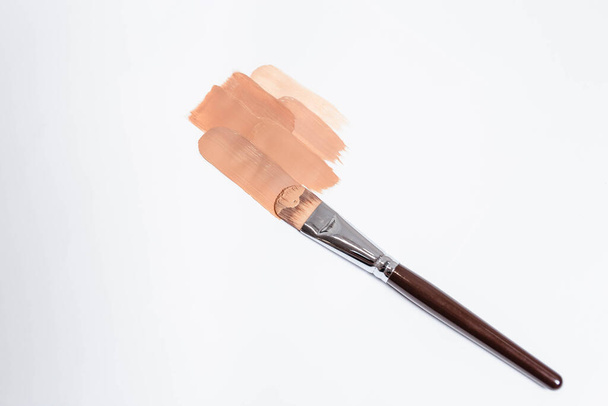 Beige liquid creamy foundation stroke smear and make-up brush isolated on white background, top view. BB cream or CC cream sample smudge, vertical. - Photo, Image