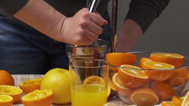 Manüel baskı ile portakal meyvesi sıkmak, yakın görüş, bir bardak taze şarap yapmak. Tahta bir masada taze portakallar, bütün ve dilimlenmiş.. - Video, Çekim