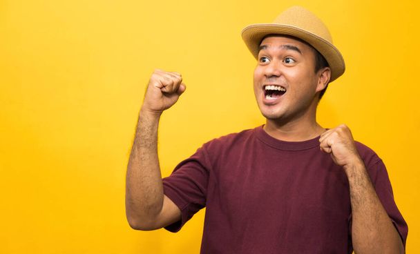 Happy young asian man celebrates with two hand in the air on yellow background. - Foto, immagini