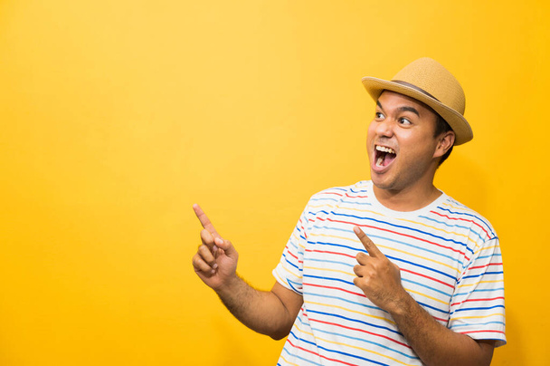 Young happy&funny asian man pointing finger on blank space for text on yellow background. - 写真・画像