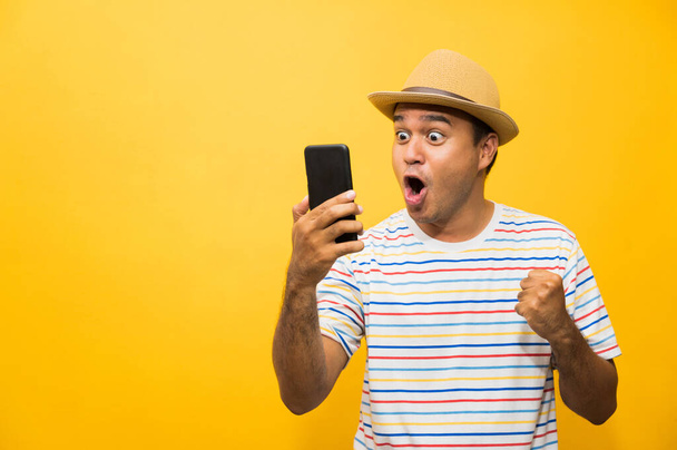 Hombre asiático feliz con su teléfono inteligente sobre fondo amarillo. hombre joven usando mirando el teléfono inteligente
. - Foto, imagen