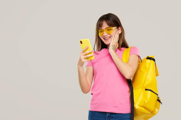 An Asian teenager girl in heart-shaped glasses holds a mobile phone in hands  on gray background. New Gadget Advertising - Foto, imagen