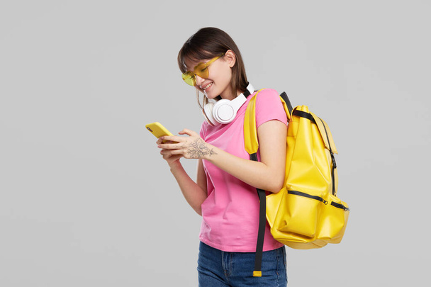 An Asian teenager girl in heart-shaped glasses holds a mobile phone in hands  on gray background. New Gadget Advertising - Foto, Bild