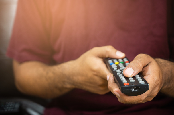 Young man holding television remote control. Hands pointing to tv set and turning it on or off select channel watching tv on his sofa at home in the living room relax. - Photo, Image