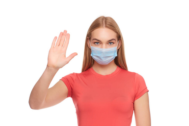 young woman in medical protective mask shows a stop gesture with hand on studio background, girl held out palm with fear, concept of quarantine measures - Foto, immagini