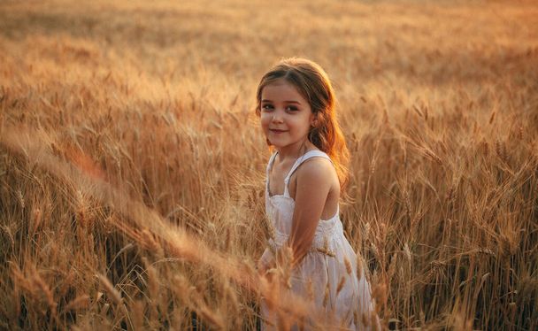 白いドレスの女の子は太陽の下で小麦の畑に立っています - 写真・画像