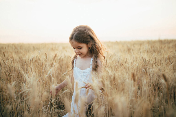 chica en un vestido blanco corre en un campo de trigo contra una puesta de sol
 - Foto, imagen