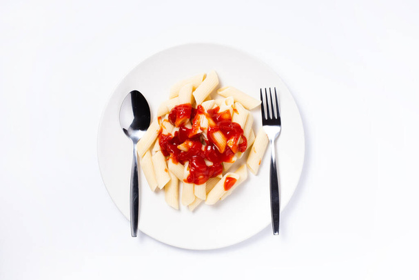 Macarrão coberto com molho de tomate em prato branco com colher e garfo no fundo branco, Vista superior
. - Foto, Imagem