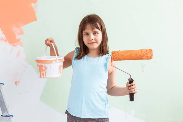 Kid standing with paint roller in hand. She is painting the wall. Redecoration, repair and repaint concept. - Foto, Imagen