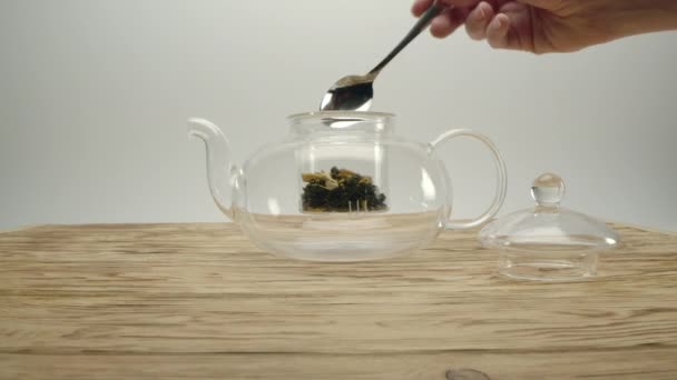 Száraz fehér tea átlátszó teáskanna, hímek kéz borítja a pot fedéllel - Felvétel, videó