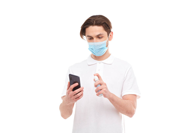 Maskeli bir Avrupalı telefonu dezenfekte ediyor. Covid-2019 salgınının konsepti. Beyaz arkaplanda izole - Fotoğraf, Görsel