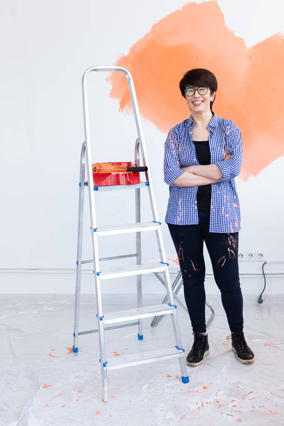 Pretty middle-aged woman with painting roller indoors. Redecoration, renovation, apartment repair and refreshment concept. - Photo, Image