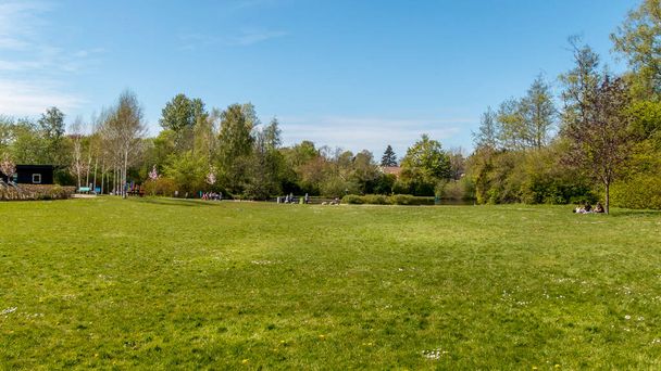 Рандерс, Дания - 09 мая 2020: The Doctor Park in Randers. Люди сидят и пьют кофе на природе. пикник в парке. озеро и лес на заднем плане. зеленые цвета и голубое небо
. - Фото, изображение
