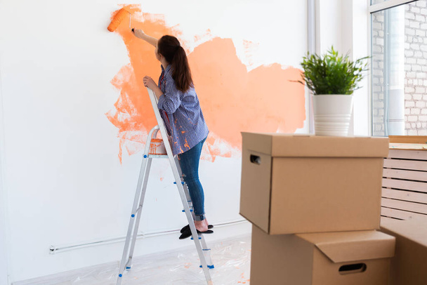 Gyönyörű nő festi a falat festékhengerrel. Egy fiatal, gyönyörű nő portréja, amint falat fest az új lakásában. Újjáépítés és felújítás koncepciója. - Fotó, kép
