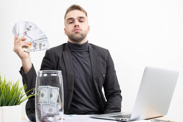 Un ragazzo con abiti da lavoro mostra i guadagni mentre è seduto sul posto di lavoro - Foto, immagini
