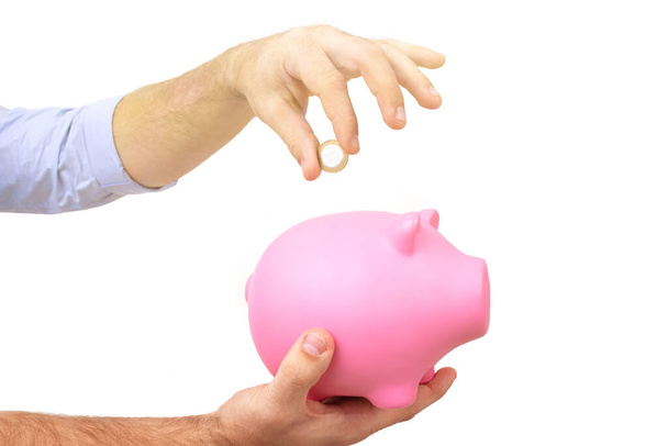 A guy in a blue shirt throws a coin into a pink piggy bank. Toned - Photo, Image