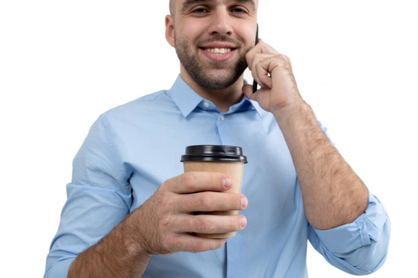 A young guy drinks coffee and talks on the phone. Start of the working day - Photo, Image