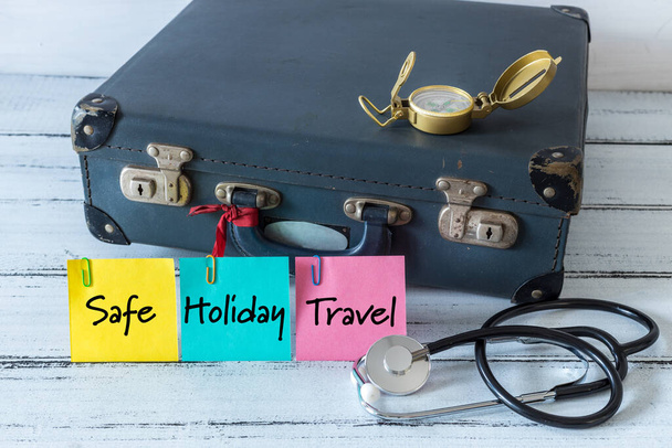  retro style suitcase with compass and medical stethoscope. Colorful sticky notes with the words "Safe, Holiday, Travel". The concept of successful holidays and family trips during a pandemic - Photo, Image