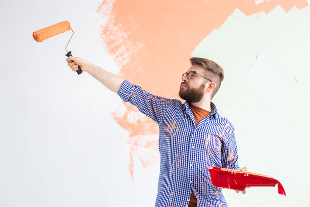 Чоловік малює стіну валиком для фарби. Портрет смішного хлопця, який малює стіну у своїй новій квартирі. Концепція реконструкції та реставрації
. - Фото, зображення