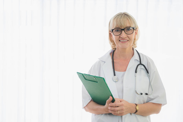 Senior woman doctor with clipboard standing near patient bed. Medical healthcare and doctor service in hospital. - Photo, image