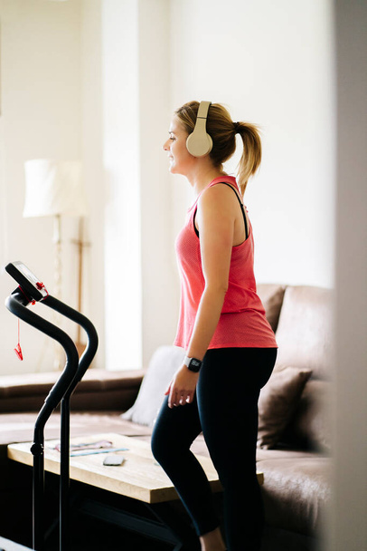 Beautiful caucasian blonde woman exercises on a treadmill in her living room - Fotoğraf, Görsel