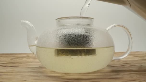 Lití vroucí vody z konvice do konvice s bílým čajem na dřevěném stole - Záběry, video